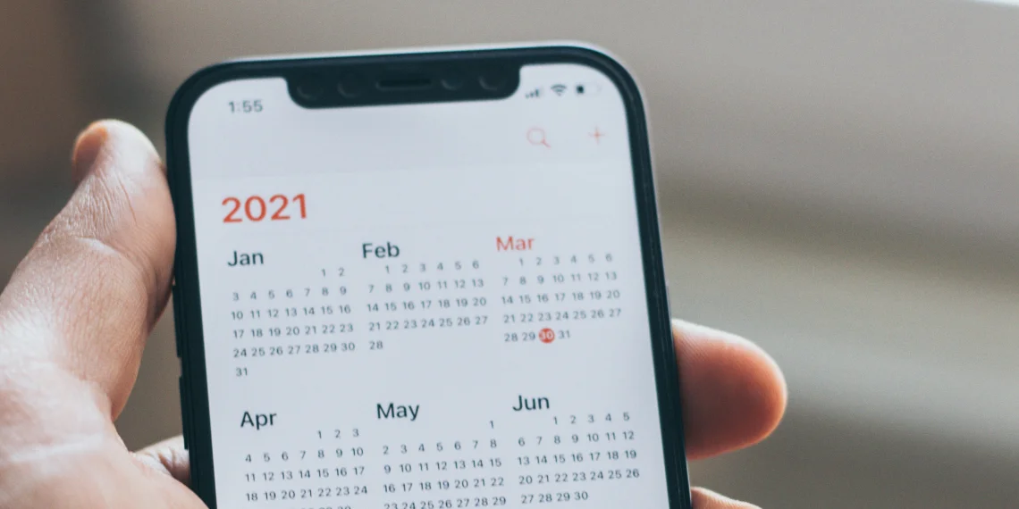 Hand holding a phone displaying a 2021 calendar screen, symbolizing planning and time considerations for university applications.