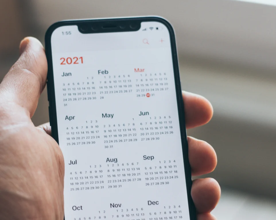 Hand holding a phone displaying a 2021 calendar screen, symbolizing planning and time considerations for university applications.